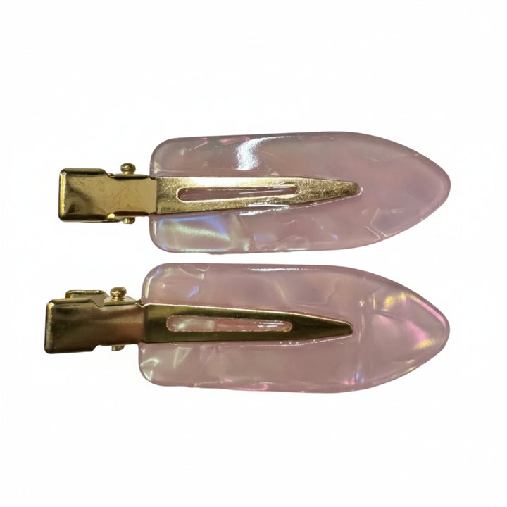 A pair of vintage-style hair claw clips with iridescent light pink resin tops and gold-tone metal clasps, shown on a plain light gray surface.