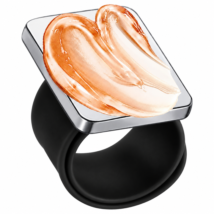 A wide black silicone ring with a square silver-toned top featuring a raised, glossy swirled cream or peach-colored sculptural detail, shown on a plain white background.