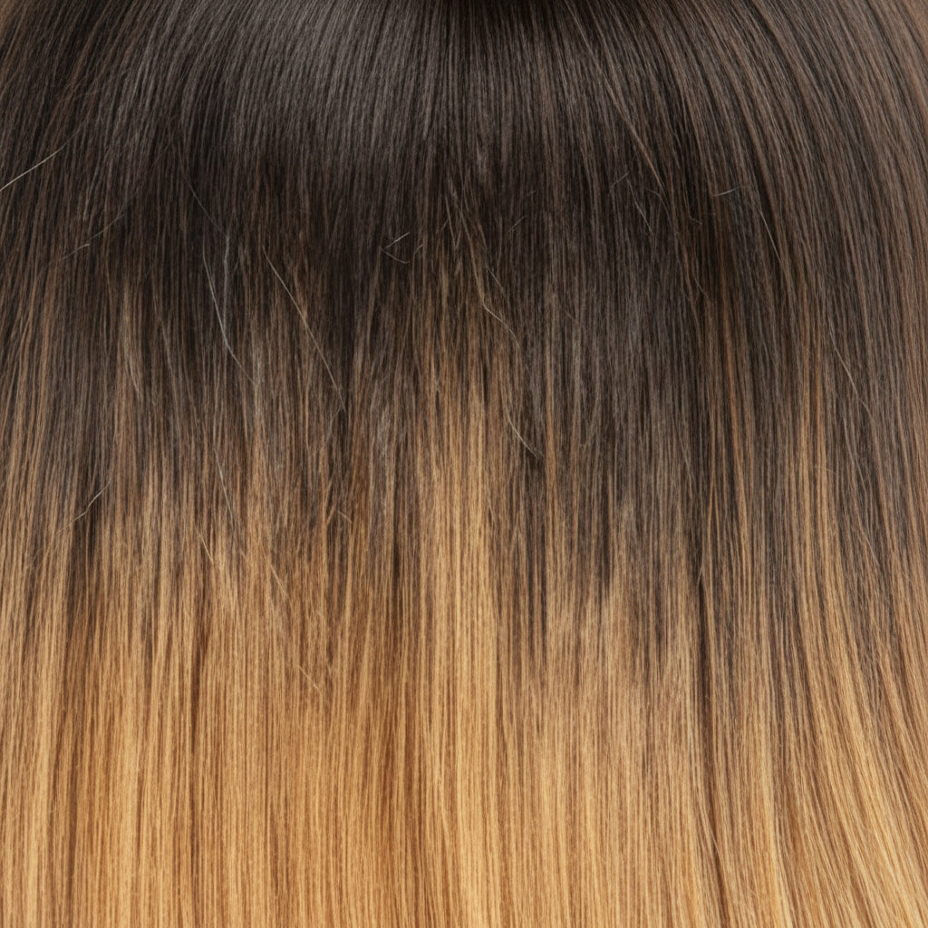 A close-up of straight hair with a dark brown to warm golden blonde ombré transition.
