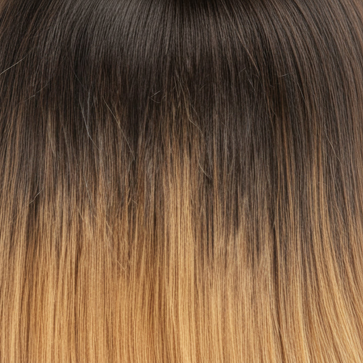 A close-up of straight hair with a dark brown to warm golden blonde ombré transition.